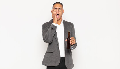 Wall Mural - young black man feeling shocked and scared, looking terrified with open mouth and hands on cheeks