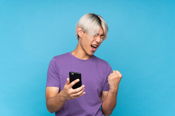 Wall Mural - Young asian man over isolated blue background with phone in victory position