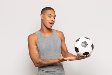 Canvas Print - young black man smiling cheerfully, feeling happy and showing a concept in copy space with palm of hand