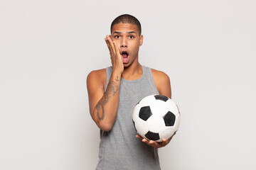 Wall Mural - young black man feeling shocked and scared, looking terrified with open mouth and hands on cheeks