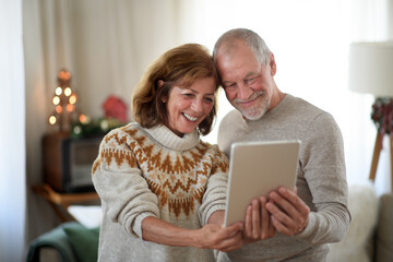 Wall Mural - Front view of senior couple with tablet indoors at home at Christmas, taking selfie.