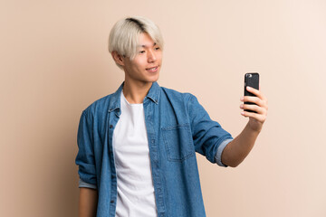 Wall Mural - Young asian man over isolated background taking a selfie with the mobile