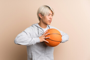 Wall Mural - Young asian man over isolated background with ball of basketball