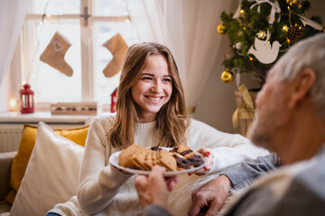 Young woman with grandfather indoors at home at Christmas, eating biscuits.