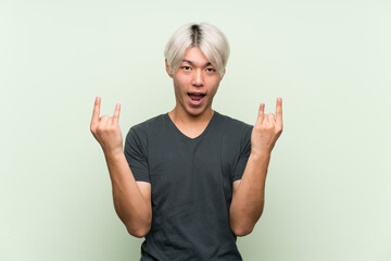 Wall Mural - Young asian man over isolated green background making rock gesture