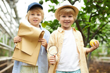 Two Kids Boys Collected Fresh Lemons In Lemonarium, Stand Together, In Greenhouse, Wearing Hat And Casual Wear, Around Trees And Plants