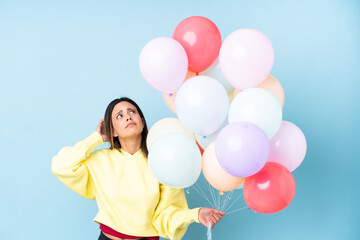 Woman holding balloons in a party over isolated blue background having doubts and with confuse face expression