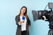 © luismolinero - Reporter woman holding a microphone and reporting news over isolated blue background