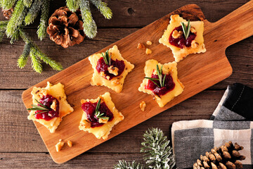 Christmas star shaped appetizers with cranberries and baked brie. Overhead view on a serving board against a wood background.