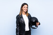 © luismolinero - Young brunette woman holding a motorcycle helmet over isolated blue background smiling a lot