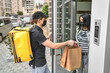 © Тарас Нагирняк - A courier with a backpack and food delivered an online order to the customer's home. The woman received her delivery near the door of her house