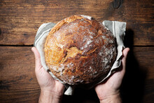 Baker's Hands Holding And Presenting Fresh Baked Loaf Of Bread