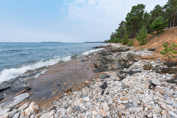 The stones, waves and trees against the backdrop of turquoise water and blue sky. Rocky eastern coast of Lake Baikal in summer. Republic of Buryatia, Russia