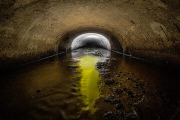 Tunnel of the old semicircular sewer drainage tunnel with gaps in the middle, from which comes a yellow light.