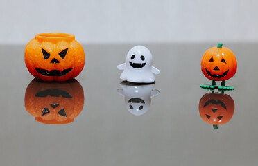 One scary orange pumpkin shaped candle, plastic white ghost toy and orange funny smiling pumpkin toy with green legs, isolated on grey background, space for text. Tradition Happy Halloween decoration.