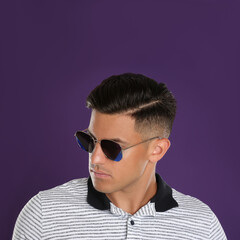 Wall Mural - Handsome man wearing sunglasses on purple background, closeup