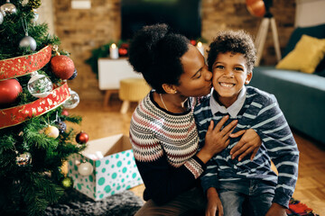 Wall Mural - Loving African American mother kissing her happy son on Christmas.