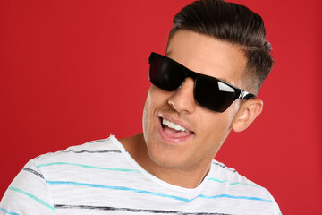 Wall Mural - Handsome man wearing sunglasses on red background, closeup