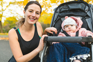 Wall Mural - Beautiful young mother with her daughter in jogging stroller outside in autumn nature
