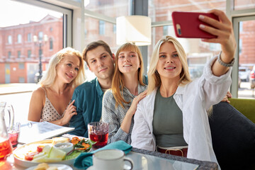 portrait of happy group of young caucasian friends taking photo on smartphone, smiling women and man spend time together in restaurant, gathered to share news, friendship concept