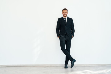 Smiling confident businessman in elegant suite posing on white wall background