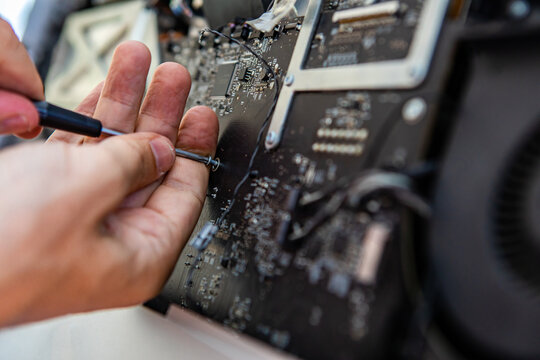 Selective focus of male technician hands holding screw driver tool to unscrew bolts in fancy desktop computer while repairing