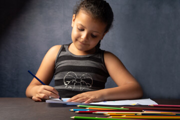 Little Brazilian girl drawing with colored pencils very happy, gray background, selective focus.