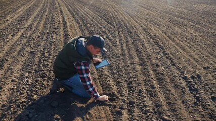 Wall Mural - man farmer red lifestyle neck with a digital tablet walking on land for sewing on a soil black field. eco farming agriculture concept. male worker studies winter dirt soil wheat crops works in field