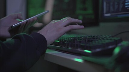 Wall Mural - unrecognizable young programmer with smartphone typing on computer keyboard. confident male caucasia