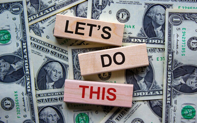 Wooden blocks with words 'lets do this'. Beautiful background from dollar bills. Copy space. Business concept.