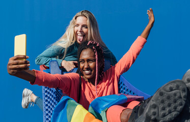 Two multiracial friends with the LGTB flag on top of a car taking pictures and having fun Concept of pride, vindication, normalization.