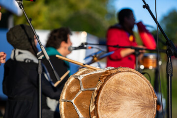 Selective focus of native sacred circle drums in cultural fiesta on stage while unrecognized musicians playing in orchestra