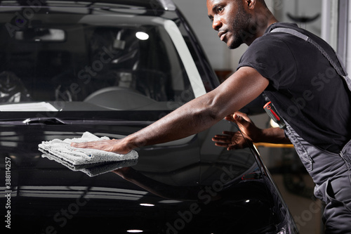 black man holds the microfiber in hand and polishes the car in auto service, do it carefully after repair