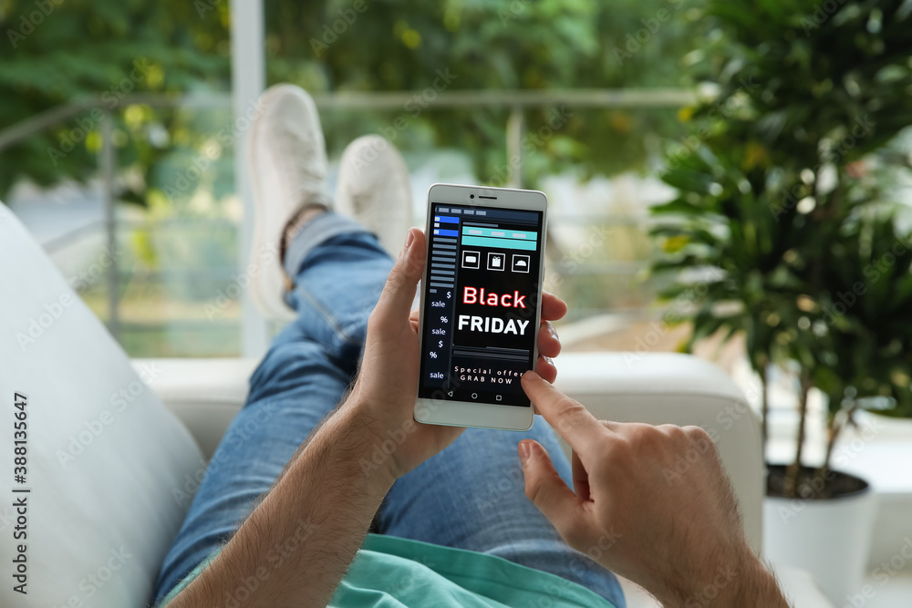 Man shopping online using smartphone on couch at home, closeup. Black Friday Sale - obrazy, fototapety, plakaty 
