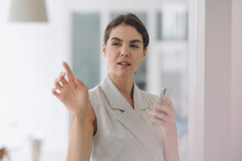 Young Woman Pointing At Glass Wall While Using Mobile Phone At Office