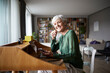 © Rainer Berg/Westend61 - Smiling active senior woman listening music while sitting on chair at home