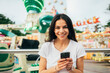 © alev/Westend61 - Close-up of smiling young woman using smart phone against amusement park ride