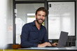 © Rainer Berg/Westend61 - Smiling man working on laptop while sitting by desk in office