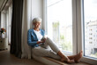 © Rainer Berg/Westend61 - Happy senior female using digital tablet while sitting on window at home