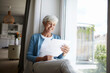 © Rainer Berg/Westend61 - Senior woman reading letter happily while sitting on window at home