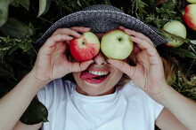 Close-up Of Cheerful Woman Holding Apples In Front Of Eyes While Lying At In Orchard