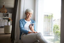 Active Senior Woman Listening To Music On Smart Phone While Sitting At Home