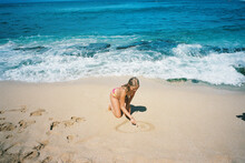 Blonde Teenager At Beach In Sand In Bikini Drawing In Sand Swimming In Ocean