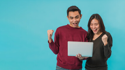 Asian young couple standing and using laptop with smiling face together isolated on blue background.Concept of happy couple working with online technology.