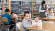 © JackF - Portrait of smiling preteen boy sitting with pile of textbooks in school library