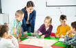 © JackF - Group of school kids with teacher sitting together around desk in classroom, playing educational tabletop game