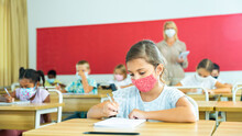 Diligent Tween Girl In Protective Mask Studying In School With Classmates. New Life Reality In Coronavirus Pandemic