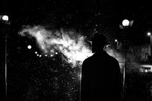 Dark Silhouette Of A Man In A Hat In The Rain On A Night Street In A City