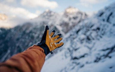 Hand winter sport glove on snow, ice and rock in the background. Snow and ice, blue sky. Winter climbing, hiking and ski touring. Point of view of an climbing tool in a hand of an alpinist.