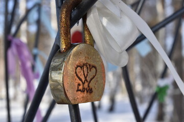 Old rusty metal lock with the inscription love and the image of two hearts hanging on the fence.